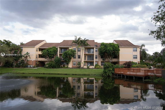 Front view of a multi-story residential building with balconies and a water body in front.