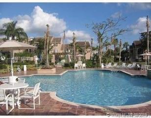 Outdoor swimming pool with surrounding lounge chairs and tables, set amidst residential buildings.