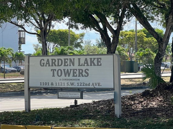 Sign for Garden Lake Towers condominium with address, surrounded by trees and vegetation.