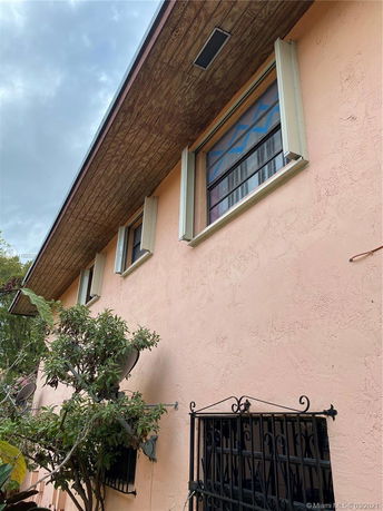 Side elevation view of a two-story house with peach-colored exterior and windows with security bars.