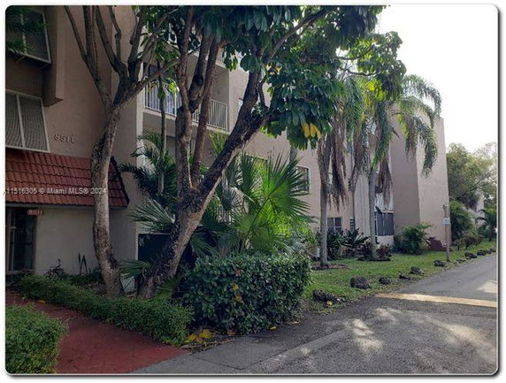 Front view of a multi-story apartment building with balconies and surrounding trees.