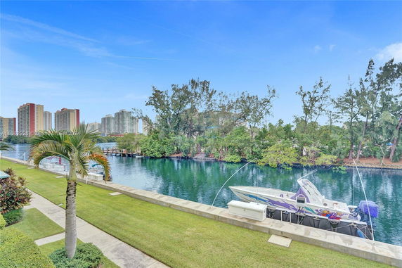 View of high-rise buildings across a body of water with greenery and a boat docked nearby.