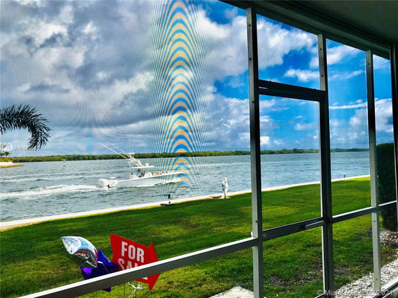 View of the water and grassy area from a building's screened balcony.