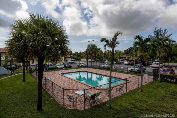 Outdoor swimming pool surrounded by a fence and palm trees.