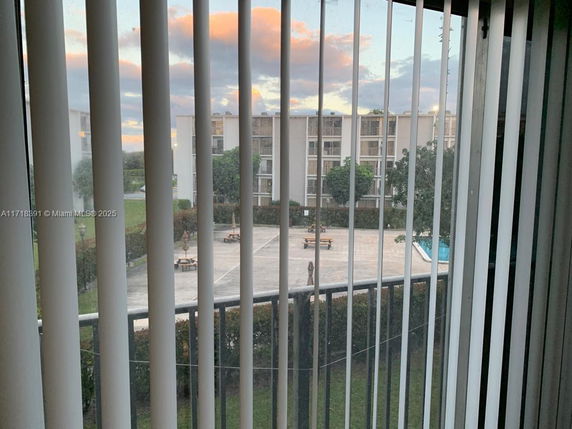 View of surrounding apartment buildings and outdoor area through vertical blinds.