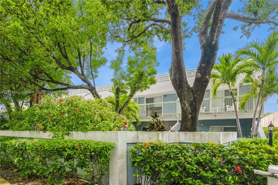 Front view of a two-story building with a balcony and surrounding greenery.