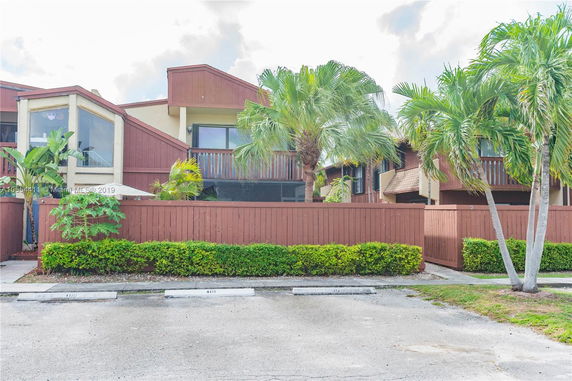 Front view of a multi-story residential building with wooden fencing and palm trees.