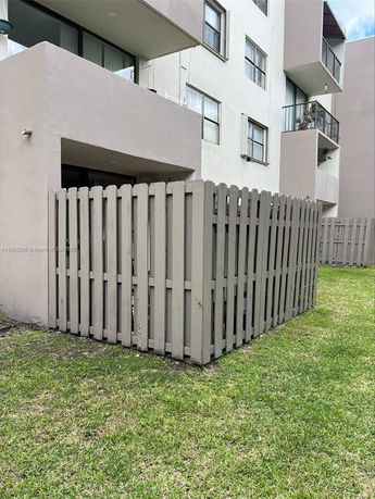 Side view of a multi-story building with balconies and a fenced area.