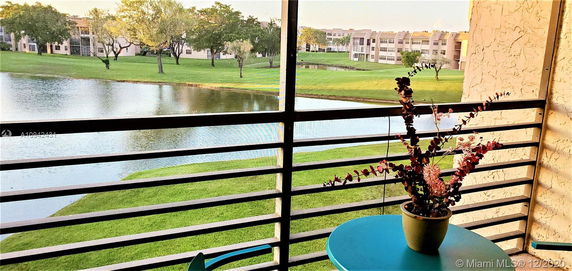 View from a balcony overlooking a pond and grassy area with trees and distant buildings.