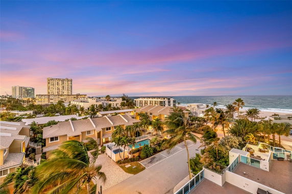 Aerial view of a residential area near the coast with palm trees and multi-story buildings during sunset.