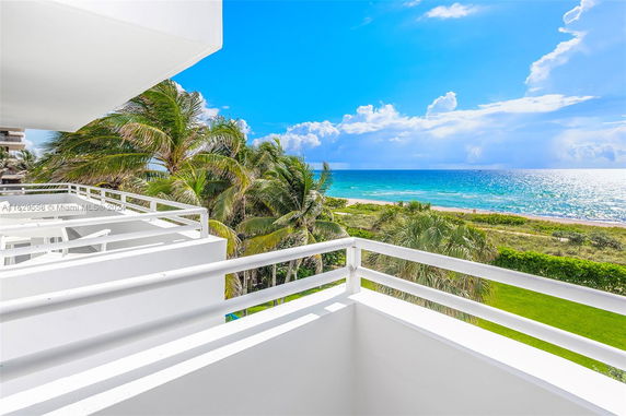View of the ocean from a white building balcony with palm trees.