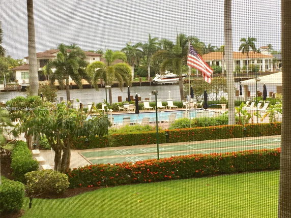 View of a pool area and waterway with houses and a docked boat in the background, seen through a screen.