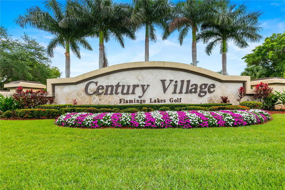 Entrance sign for Century Village with landscaping and palm trees.