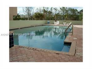 Outdoor swimming pool with paved surroundings and some seating.