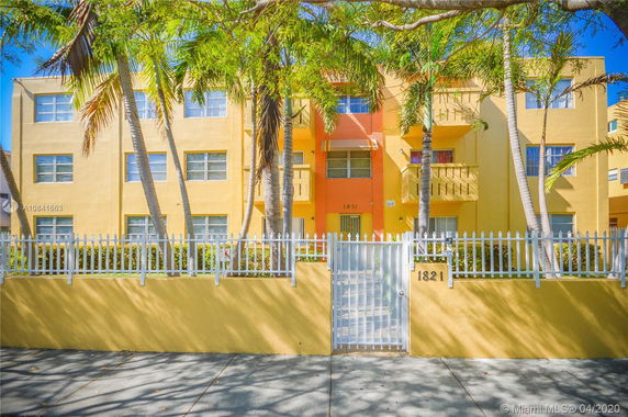 Front view of a three-story building with a gated entrance and palm trees.