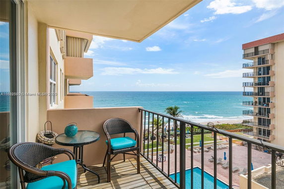 View from a balcony overlooking the ocean and a beachside pool area, with buildings in the background.