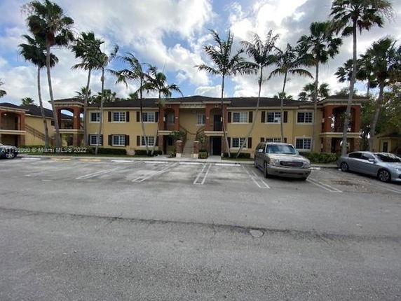 Front view of a two-story building with palm trees and a parking area.