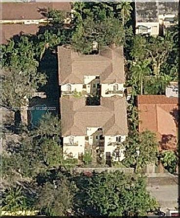 Aerial view of a building with a beige roof surrounded by trees and neighboring houses.