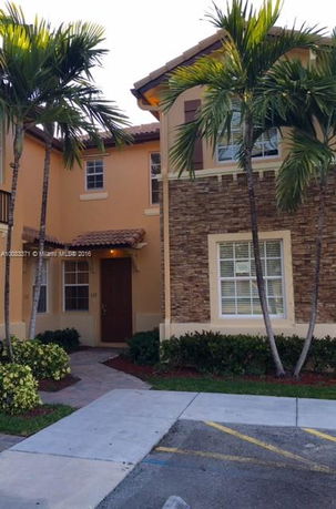 Front view of a two-story house with stone accents and palm trees.