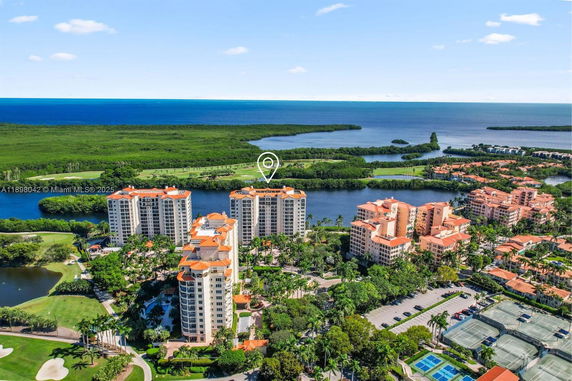 Aerial view of a coastal residential complex with multiple high-rise buildings, tennis courts, and surrounding greenery overlooking the ocean.