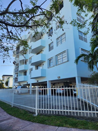 Front view of a multi-story building with balconies and a fenced parking area.
