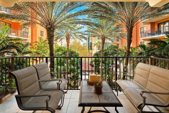 View from a balcony with seating, overlooking palm trees and nearby buildings.