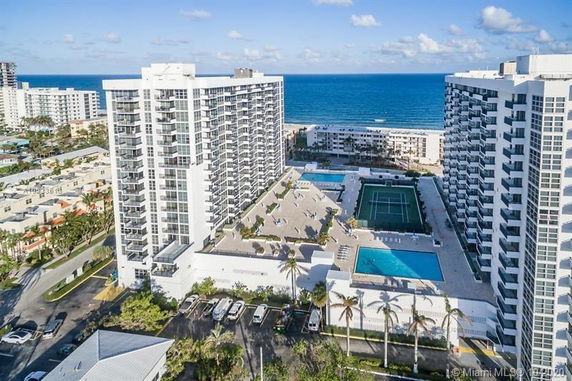 Aerial view of high-rise buildings near the ocean with swimming pools and a tennis court.