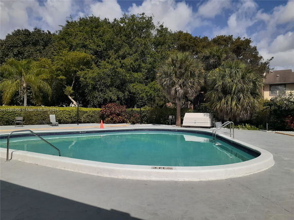 Outdoor swimming pool area surrounded by trees and lounge chairs.
