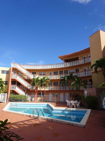Outdoor swimming pool area in front of a multi-story building with curved balconies.