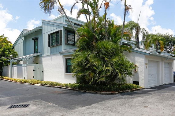 Front view of a two-story house with a garage and tropical landscaping.