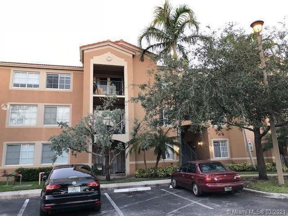Front view of a three-story apartment building with palm trees and parking area.