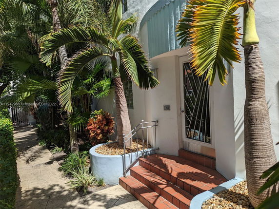Front view of a building entrance with plants and trees.