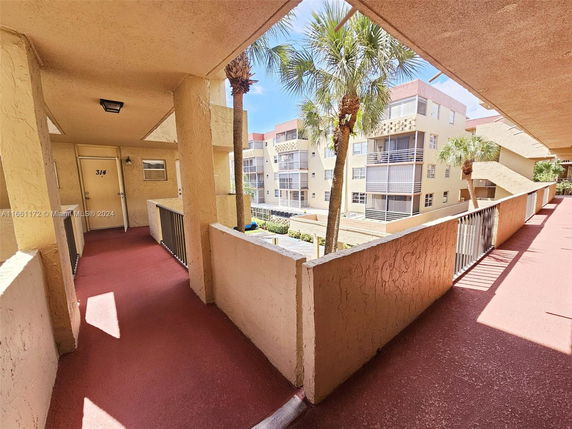 View from a corridor showcasing a multi-story residential building with balconies and palm trees.