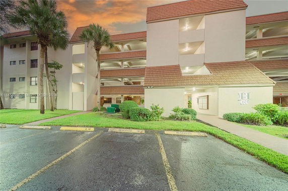 Front view of a multi-story residential building with balconies and parked cars.