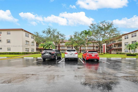 Parking lot with several cars in front of a multi-story building.