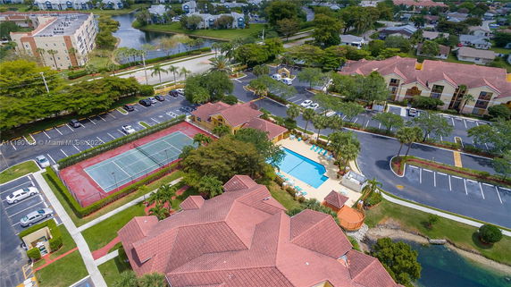 Aerial view of a residential area with a swimming pool, tennis court, and parking spaces.
