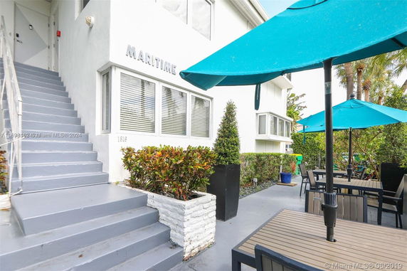 Front view of a building with stairs and patio furniture under umbrellas.