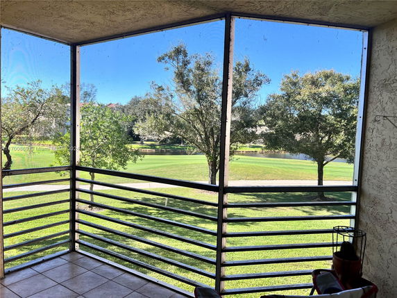 View from a screened balcony overlooking a grassy area with trees and a pond.
