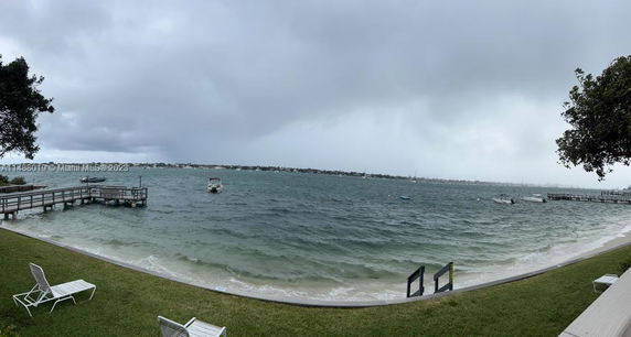 Panoramic view of a waterfront area with a dock and chairs on a grassy shore.
