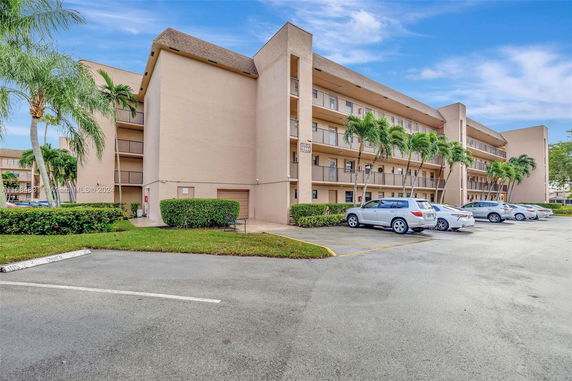 Front view of a four-story apartment building with balconies and a parking area.