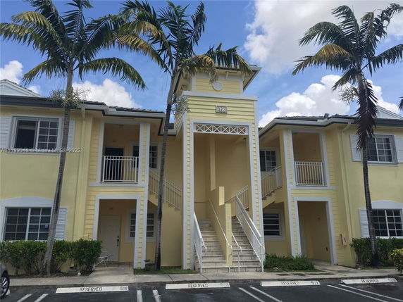 Front view of a two-story building with yellow exterior and white accents, featuring staircases and balconies.