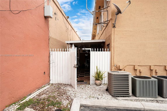 View of the side of a building with a gate and air conditioning units.