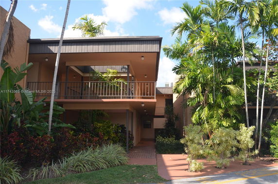 Front view of a two-story house with balcony and lush greenery.
