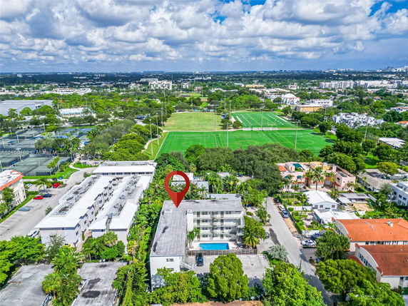 Aerial view of a residential area with surrounding greenery and sports fields.