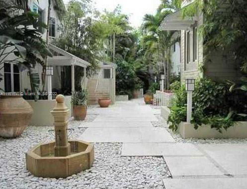 Pathway view between buildings with a small fountain and surrounding vegetation.
