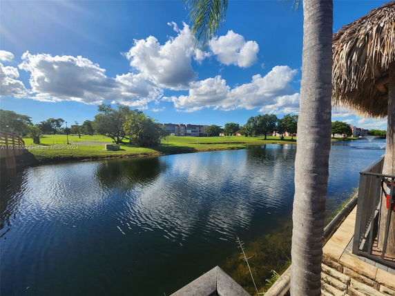 View of a lake with surrounding trees and distant buildings under a blue sky with clouds.