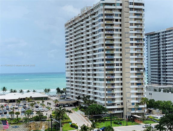 View of high-rise building near the ocean with surrounding parking and green areas