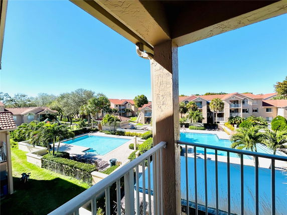 View from a balcony overlooking a swimming pool and residential buildings with tiled roofs.