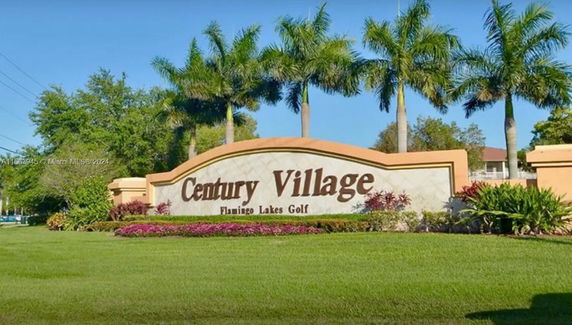 Entrance sign for Century Village with surrounding landscaping and palm trees.
