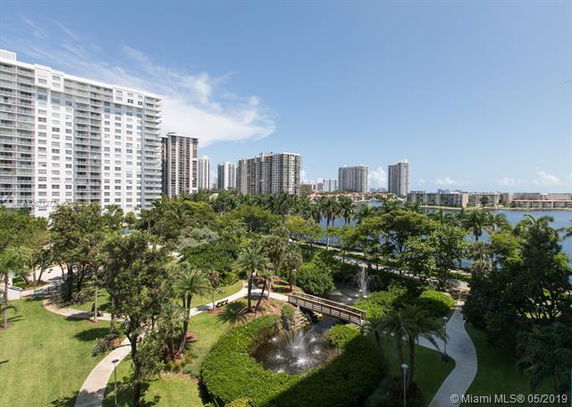 View of high-rise buildings near a lake with lush green park areas and trees in the foreground.